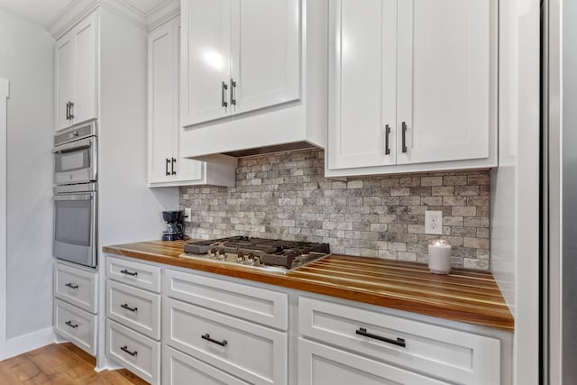 kitchen featuring appliances with stainless steel finishes, wood counters, white cabinetry, backsplash, and light hardwood / wood-style flooring