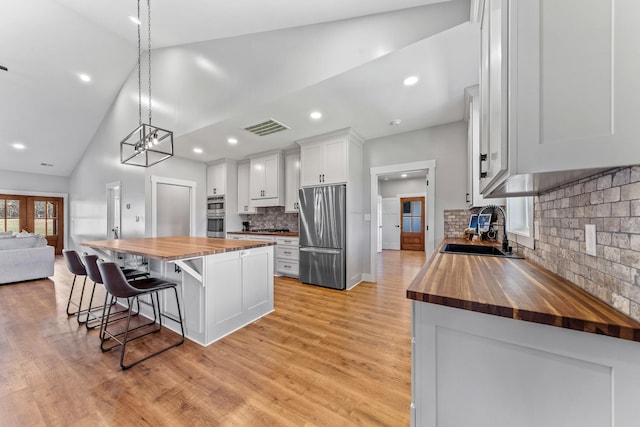 kitchen with wooden counters, a kitchen island, sink, white cabinetry, and stainless steel appliances