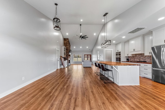 kitchen featuring stainless steel appliances, white cabinets, wooden counters, and high vaulted ceiling