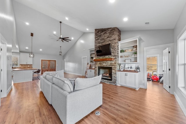 living room featuring ceiling fan, light hardwood / wood-style flooring, a stone fireplace, and high vaulted ceiling