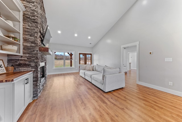 living room with light wood-type flooring, a stone fireplace, and high vaulted ceiling