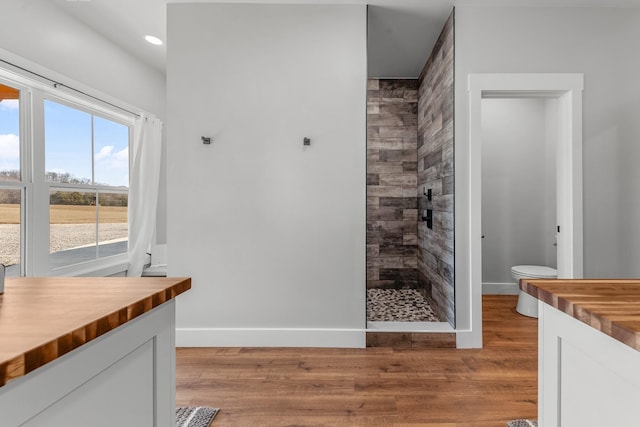 bathroom with toilet, a tile shower, wood-type flooring, and vanity