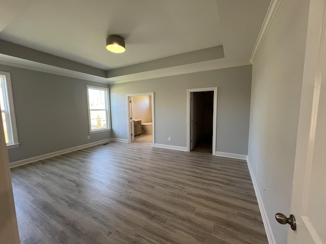 unfurnished bedroom featuring dark wood-type flooring, a walk in closet, crown molding, connected bathroom, and a closet