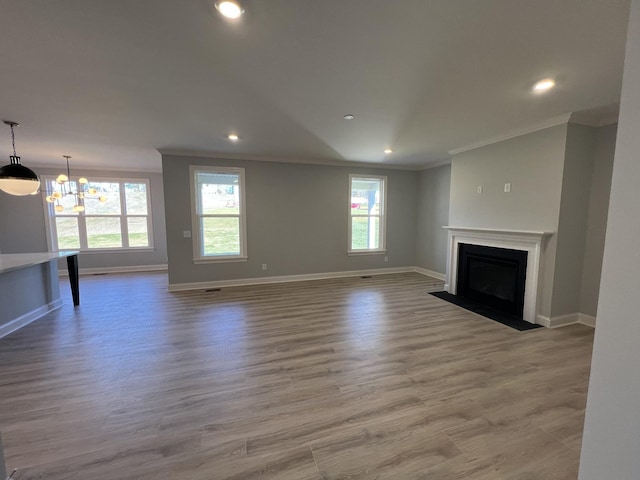 unfurnished living room with light hardwood / wood-style flooring, a healthy amount of sunlight, crown molding, and an inviting chandelier