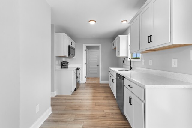 kitchen with white cabinets, appliances with stainless steel finishes, light hardwood / wood-style floors, and sink