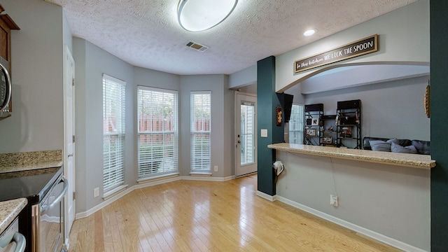 kitchen with dishwasher, light hardwood / wood-style floors, light stone counters, and a textured ceiling