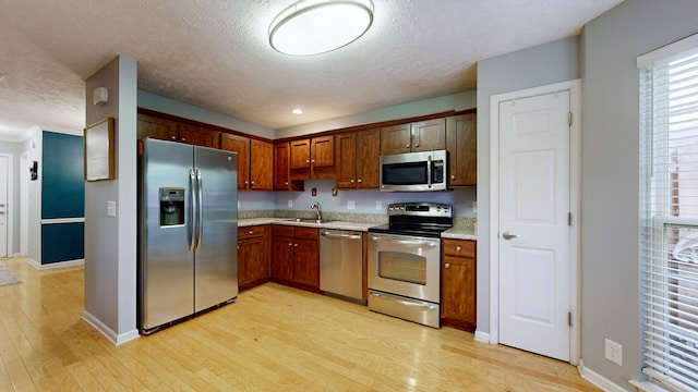 kitchen featuring appliances with stainless steel finishes, a textured ceiling, light hardwood / wood-style flooring, and sink