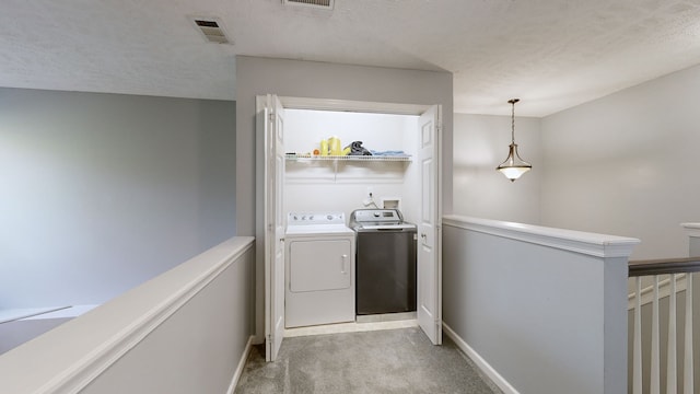 washroom featuring washing machine and dryer, light colored carpet, and a textured ceiling