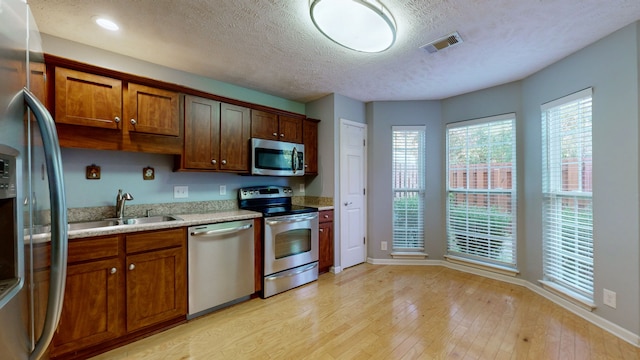 kitchen with sink, light hardwood / wood-style flooring, light stone countertops, a textured ceiling, and stainless steel appliances