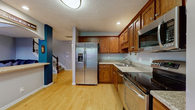 kitchen featuring sink, light wood-type flooring, a textured ceiling, appliances with stainless steel finishes, and light stone counters