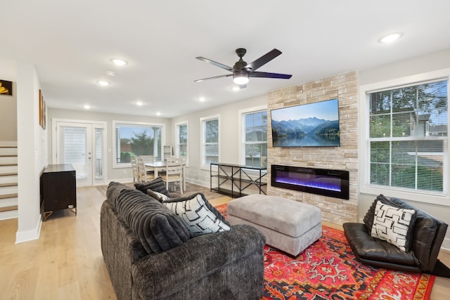 living room featuring light hardwood / wood-style floors, ceiling fan, and a stone fireplace