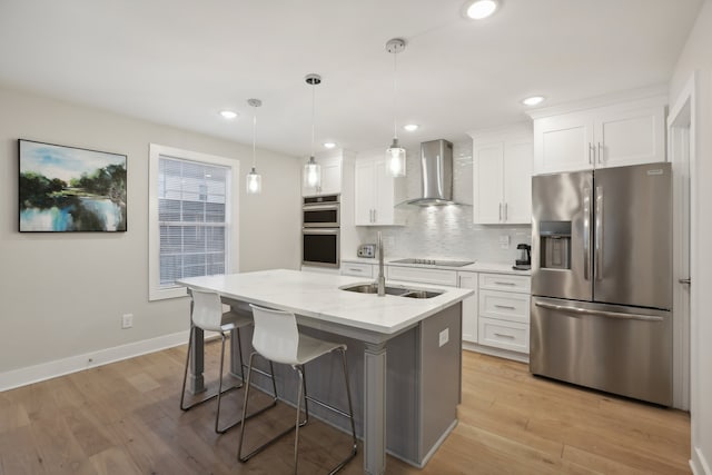 kitchen with light stone countertops, appliances with stainless steel finishes, wall chimney exhaust hood, white cabinetry, and a center island with sink