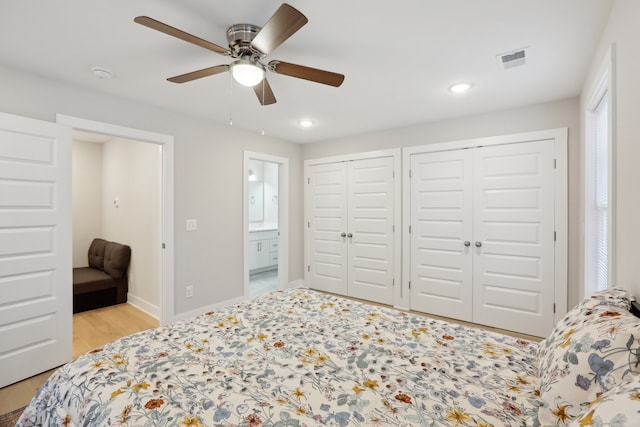 bedroom featuring light hardwood / wood-style floors, connected bathroom, two closets, and ceiling fan