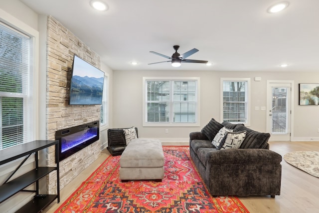 living room with ceiling fan, light hardwood / wood-style flooring, and a stone fireplace