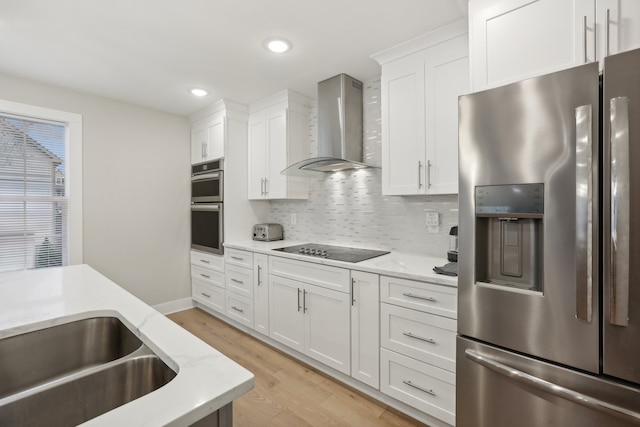 kitchen with wall chimney range hood, stainless steel appliances, white cabinetry, and decorative backsplash