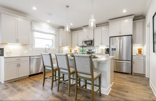 kitchen with light wood-type flooring, decorative light fixtures, a kitchen island, white cabinetry, and stainless steel appliances