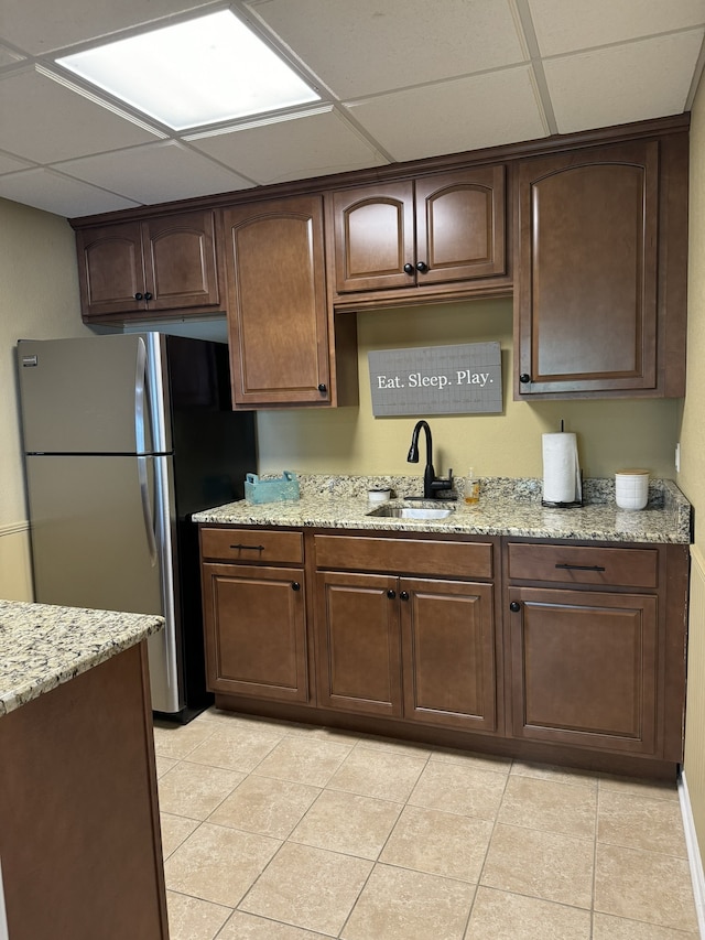 kitchen with light stone countertops, stainless steel fridge, a drop ceiling, sink, and light tile patterned floors