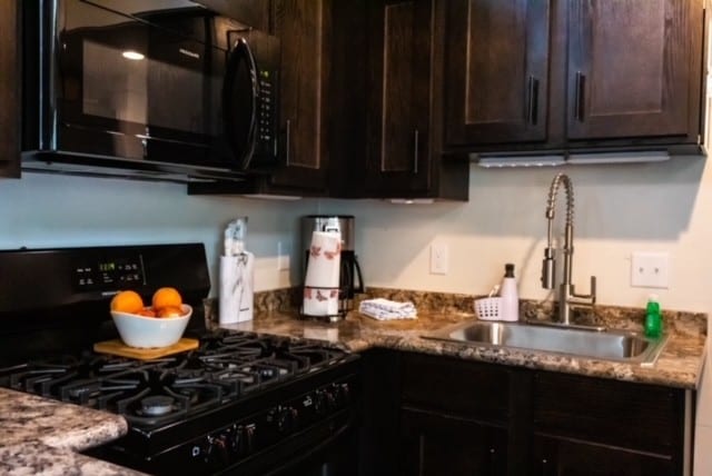 kitchen with black appliances, dark brown cabinets, light stone counters, and sink