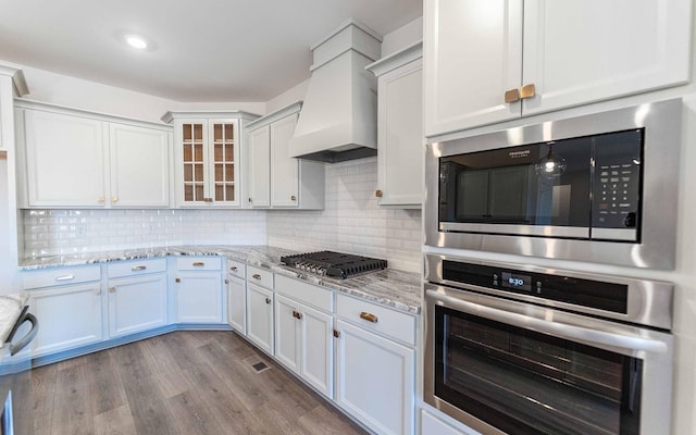 7938 Pine St, Fairview, TN 37062 - kitchen with stainless steel appliances, custom exhaust hood, glass insert cabinets, wood finished floors, and white cabinets