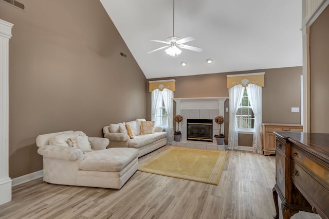 living room featuring a tile fireplace, light wood-type flooring, high vaulted ceiling, and ceiling fan