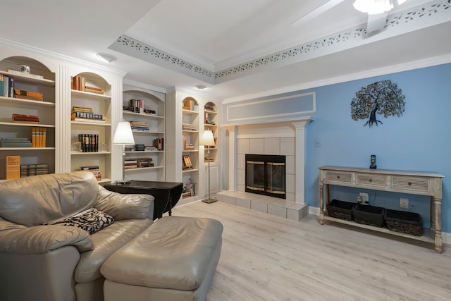 living room featuring built in features, crown molding, a tray ceiling, a fireplace, and light wood-type flooring