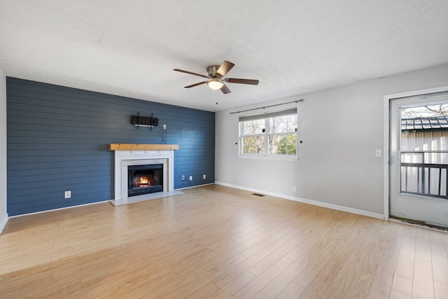 unfurnished living room featuring ceiling fan, light wood-type flooring, a textured ceiling, and wooden walls