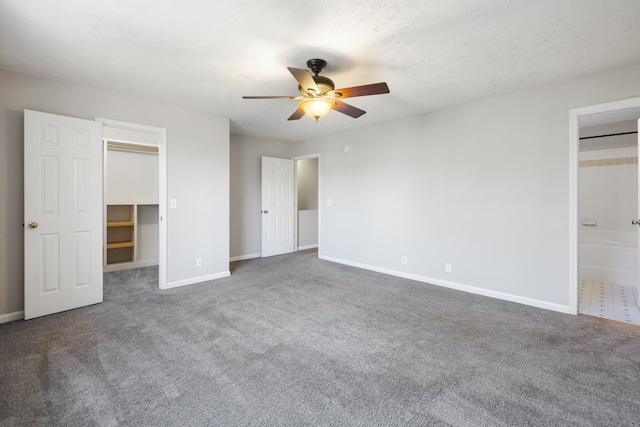 unfurnished bedroom featuring ensuite bath, ceiling fan, a textured ceiling, a walk in closet, and dark carpet