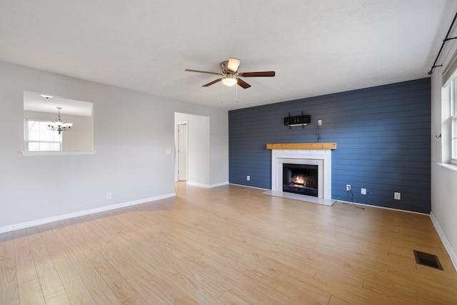 unfurnished living room with ceiling fan with notable chandelier, light hardwood / wood-style floors, and wooden walls