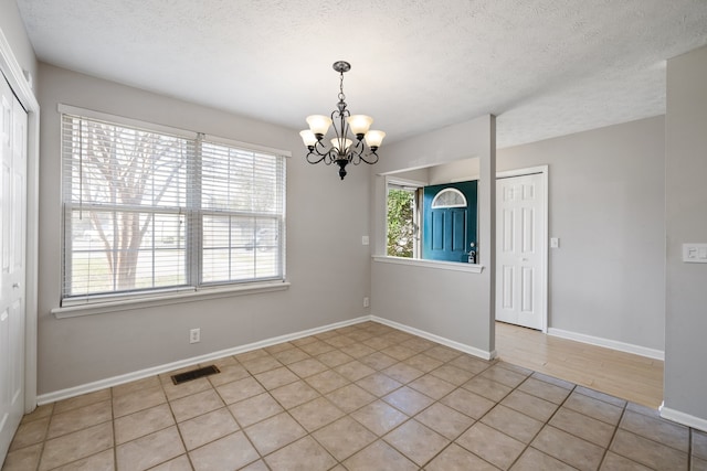 empty room featuring a notable chandelier, plenty of natural light, light tile patterned floors, and a textured ceiling