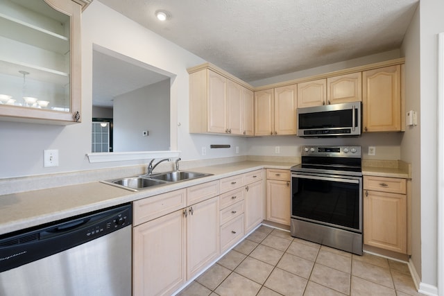 kitchen featuring appliances with stainless steel finishes, a textured ceiling, light brown cabinetry, and sink