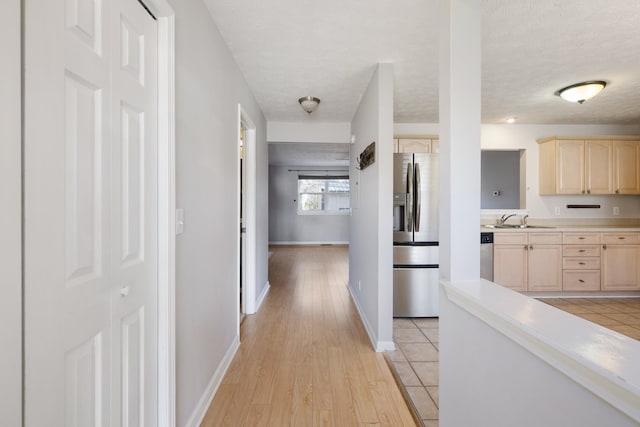 corridor with a textured ceiling, light hardwood / wood-style floors, and sink