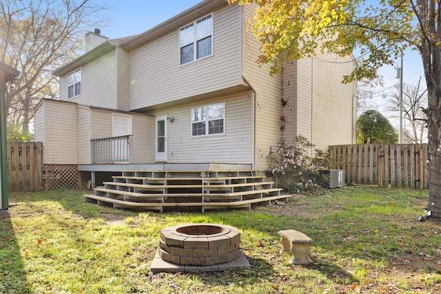 back of property featuring a lawn, a wooden deck, a fire pit, and central AC