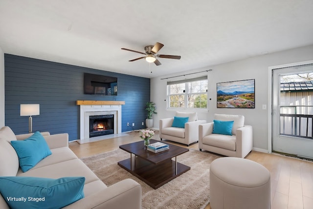 living room with ceiling fan, wood walls, and light wood-type flooring