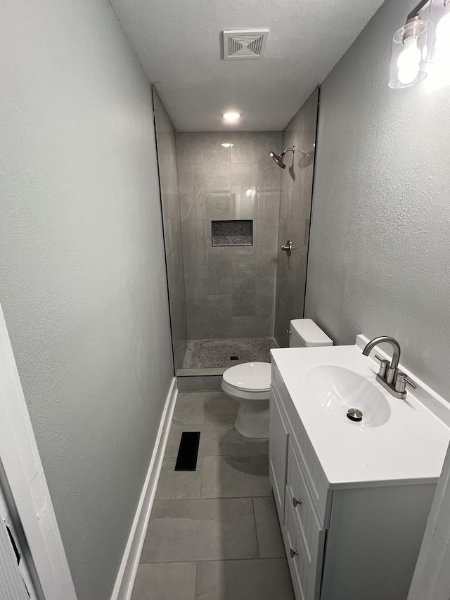 bathroom featuring tiled shower, tile patterned flooring, vanity, and toilet