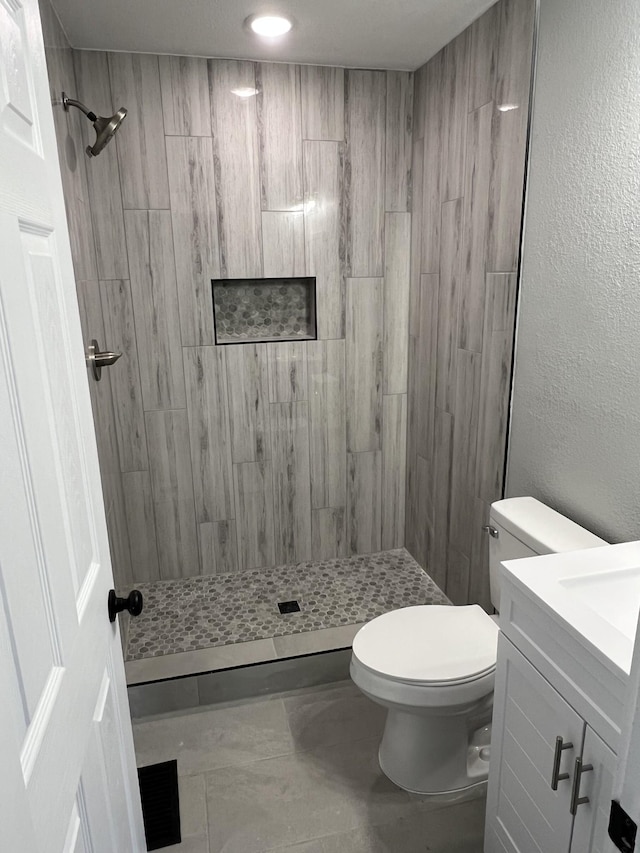 bathroom with vanity, toilet, and a tile shower