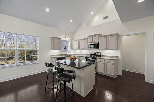 kitchen featuring high vaulted ceiling, stainless steel appliances, a kitchen island, gray cabinets, and dark wood-style floors