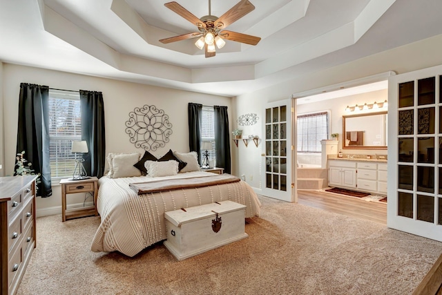 carpeted bedroom with ensuite bath, ceiling fan, french doors, and a tray ceiling