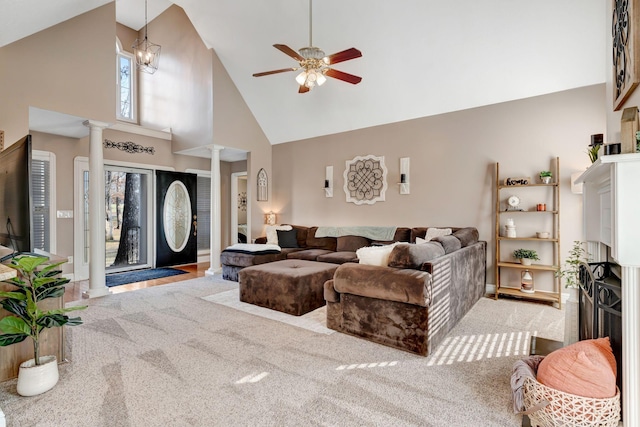 carpeted living room with ceiling fan with notable chandelier, decorative columns, and high vaulted ceiling