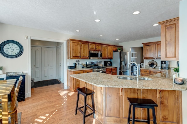 kitchen featuring kitchen peninsula, a kitchen bar, light stone counters, stainless steel appliances, and sink