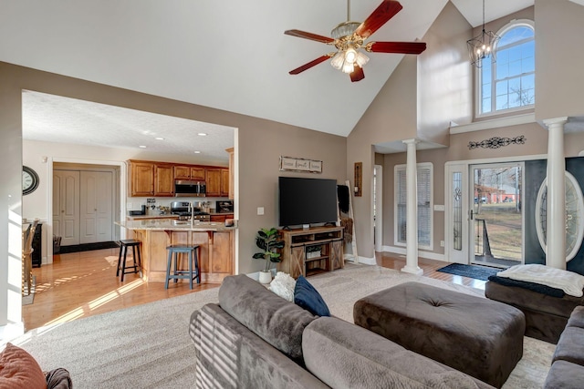 living room featuring decorative columns, high vaulted ceiling, and ceiling fan with notable chandelier