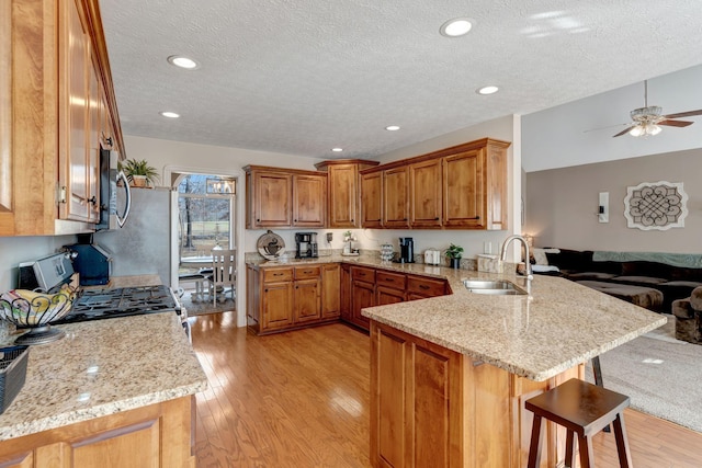 kitchen featuring kitchen peninsula, a kitchen bar, light wood-type flooring, stainless steel appliances, and sink