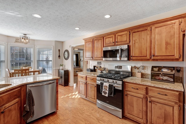 kitchen featuring light stone countertops, appliances with stainless steel finishes, a textured ceiling, and light hardwood / wood-style flooring