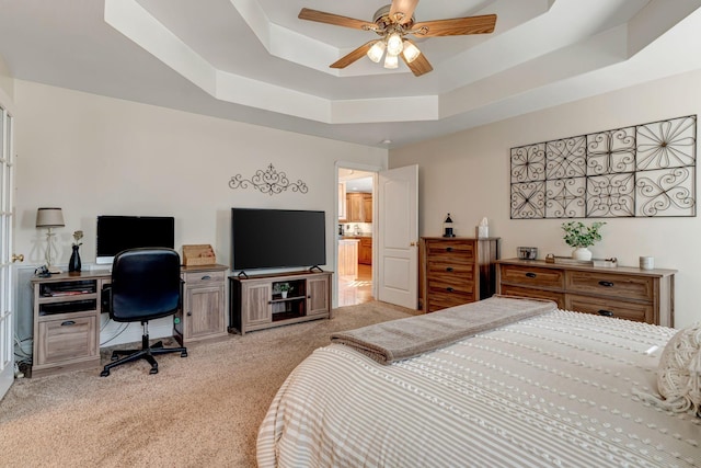 bedroom with a tray ceiling, ceiling fan, ensuite bathroom, and light colored carpet