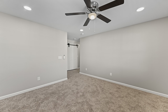 spare room featuring carpet flooring, a barn door, and ceiling fan