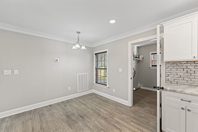 unfurnished dining area with a notable chandelier, light wood-type flooring, and crown molding