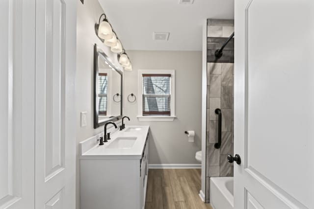 full bathroom featuring hardwood / wood-style floors, vanity, tiled shower / bath combo, and toilet