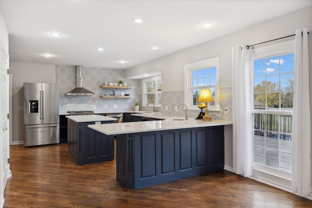 kitchen featuring kitchen peninsula, stainless steel refrigerator with ice dispenser, tasteful backsplash, wall chimney range hood, and dark hardwood / wood-style floors