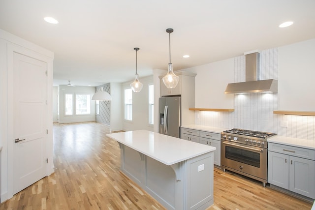 kitchen featuring gray cabinetry, a kitchen breakfast bar, wall chimney range hood, light hardwood / wood-style floors, and stainless steel appliances