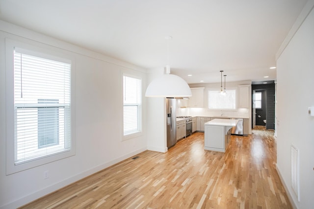 kitchen with sink, a center island, stainless steel appliances, hanging light fixtures, and light hardwood / wood-style floors