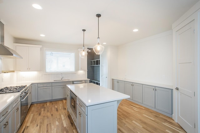 kitchen with sink, wall chimney exhaust hood, hanging light fixtures, a kitchen island, and light wood-type flooring